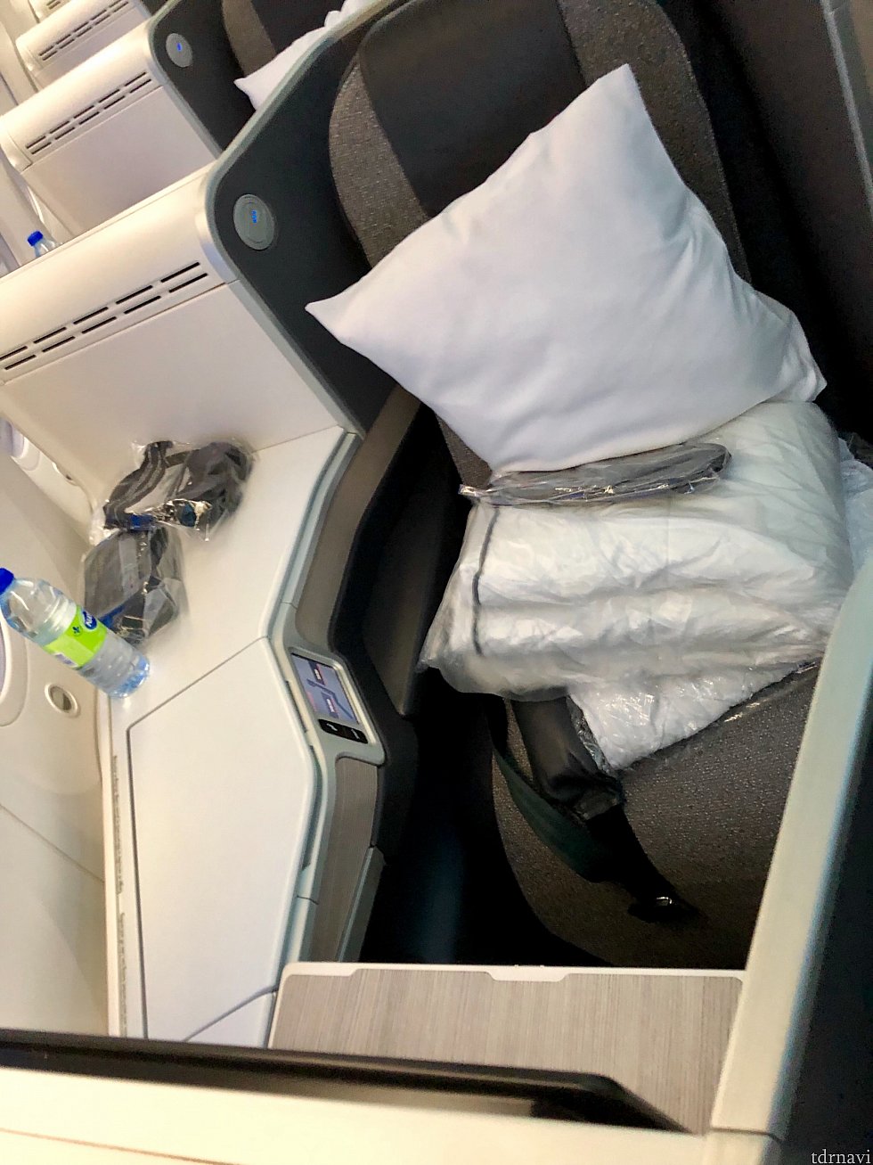 こちらがフルフラットベッドにもなる座席。シートベルトにもパッドが入っていて、席にはシートカバー、掛布団、枕、水ボトル、スリッパ、アメニティーセット、ヘッドセットが置いてありました。